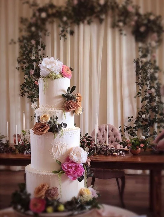 A floral wedding cake beneath a decorated reception arch